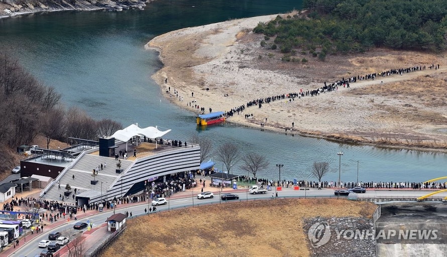 A high-angle wide shot of a long line of tourists waiting for the ferry to Cheongnyeongpo in Yeongwol, the primary filming location of 'The King's Warden'.