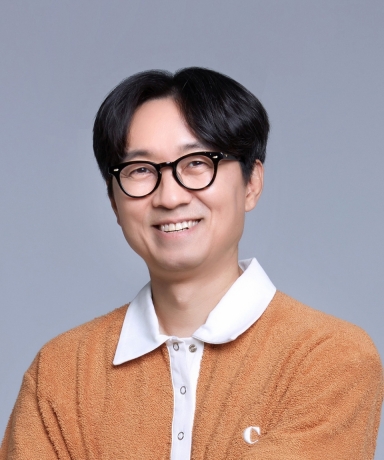 A professional portrait of Korean film director Jang Hang-jun, smiling warmly and wearing glasses, representing his role in the show 'The King's Warden'.