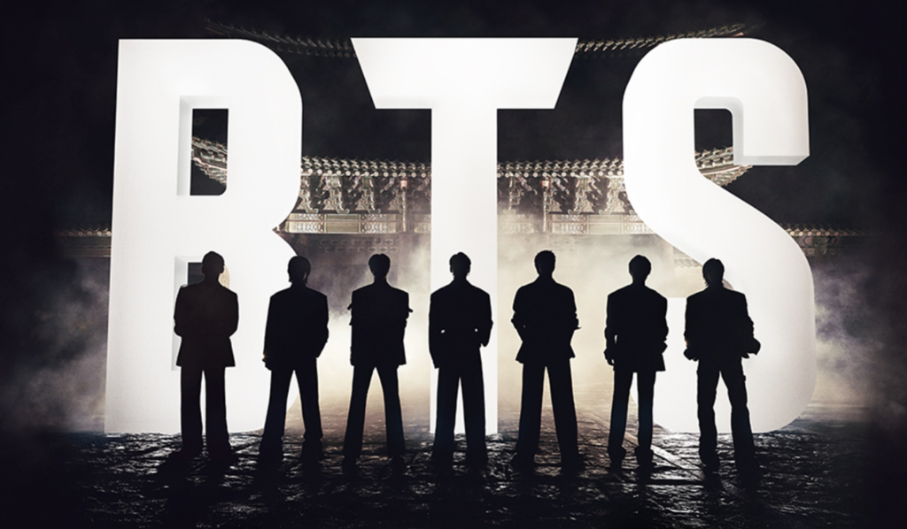 Silhouettes of the seven BTS members standing in front of the illuminated Gwanghwamun Gate with a large 'BTS' logo.