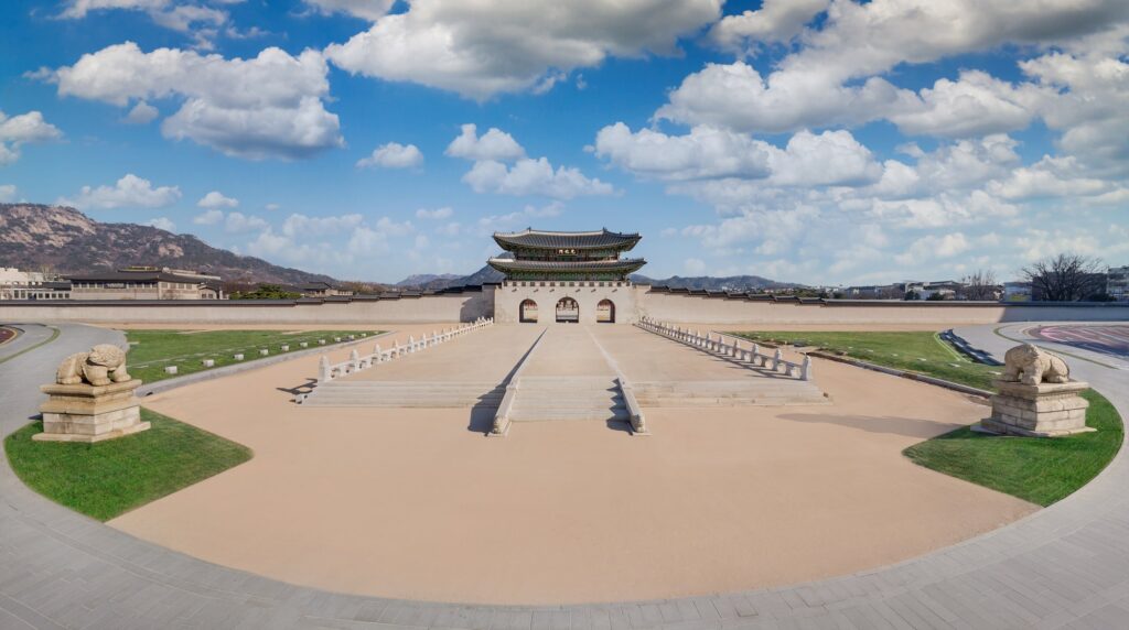 A wide panoramic view of Gwanghwamun Gate and the newly restored Woldae ceremonial stage under a blue sky with white clouds.