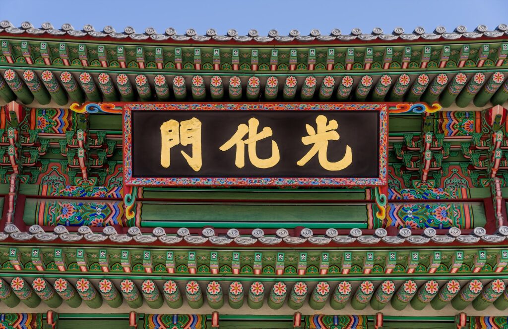 Close-up of the Gwanghwamun Gate signboard with gold Hanja characters on a black background, framed by colorful traditional Dancheong patterns.