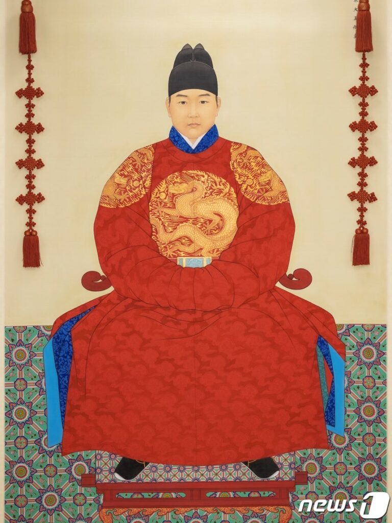 An official Korean standard portrait of King Danjong sitting on a throne. He is wearing a bright red royal robe (Gollyongpo) with a golden dragon emblem on the chest and a traditional black winged cap (Ikseongwan).