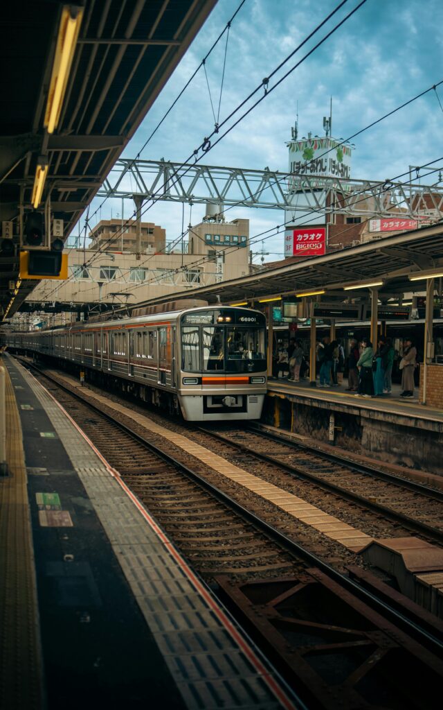 ​A bright yellow Tokyo Metro Ginza Line train stopped at an underground station. The train has a retro-modern design with a rounded front and a dark window area. The platform is clean and modern with glass screen doors. Clear Japanese and English signage is visible on the station walls.