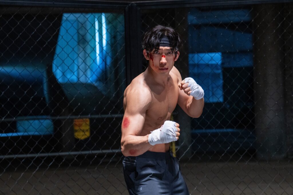 Actor Lee Sang-yi with a head band and boxing wraps in an intense fighting stance, capturing a gritty scene from the Netflix drama Bloodhounds Season 2.